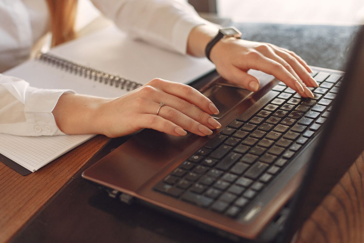 The image shows a notebook and a girl's hand typing on the laptop indicating that creating a financial GPS makes staying on course fun and rewarding.