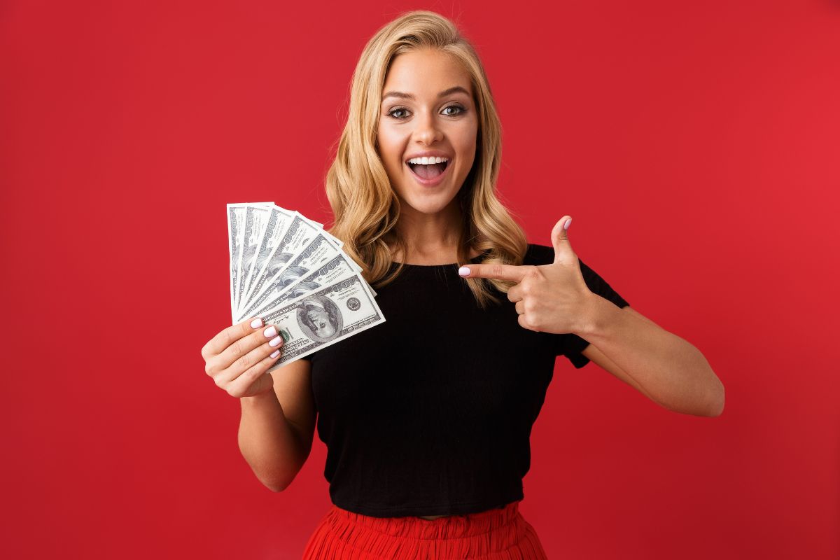 The image tells about a girl holding dollar bills and pointing which means setting money milestones with excitement keeps you motivated without undoing your progress.