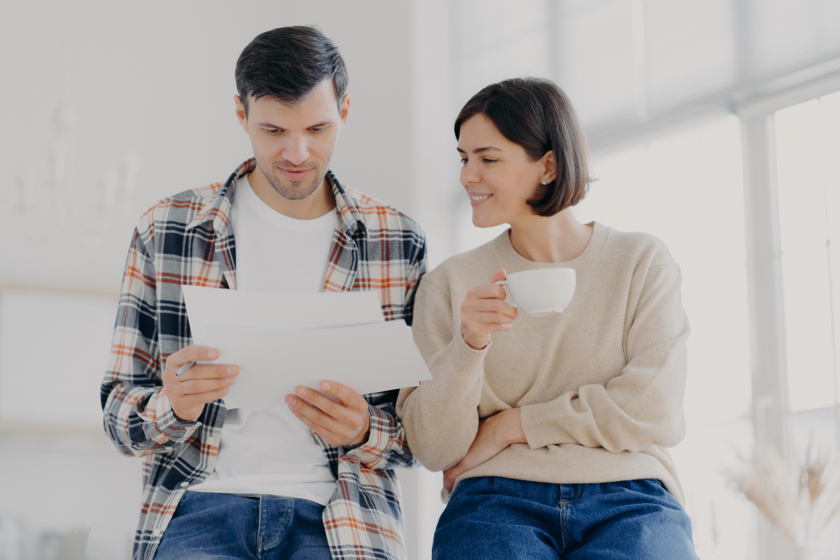 The image shows a couple looking at the papers while having a coffee indicating that using an accountability partner keeps you motivated to check in on your progress and makes reaching financial goals easier.