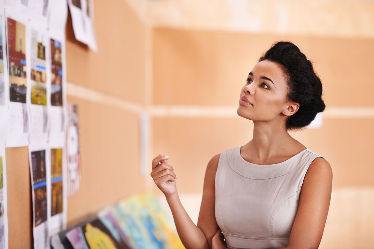 The image shows a girl looking at the wall of pictures which means visualize the day you reach your goal makes daily sacrifices easier.
