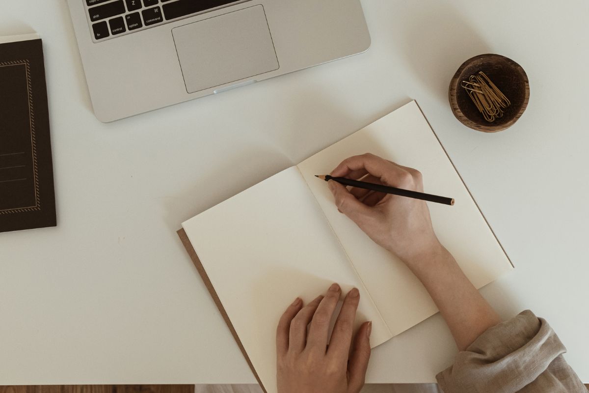 The picture shows a laptop, pins on the container, and a girl's hand and writing on the notebook referring to creating a dream job statement and saying it daily to keep yourself focused and make it feel real.