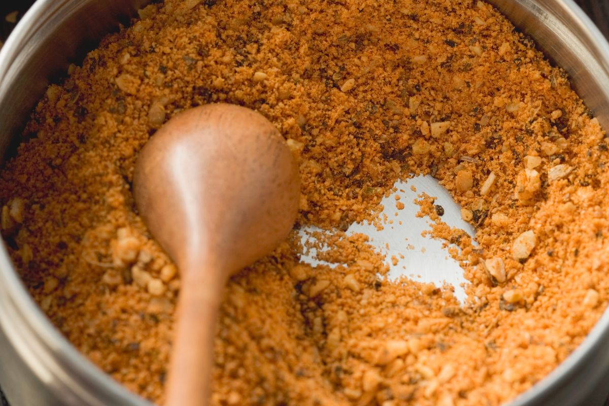 The picture shows a bowl with spices and a spoon which means making your seasoning mixes saves money on groceries while cutting out unnecessary additives.