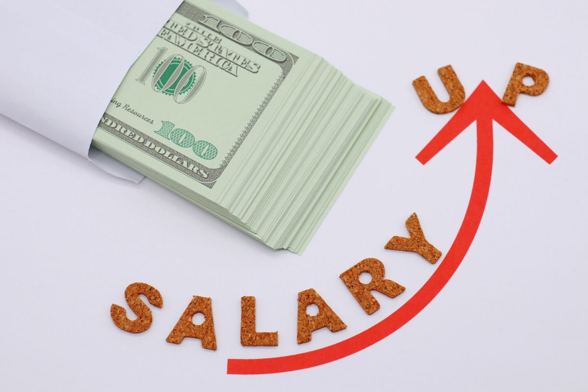 The image tells about an envelope with dollar bills, an arrow up, and a letter which means to set a salary goal that feels too big to become motivated and feels out of reach but exciting.