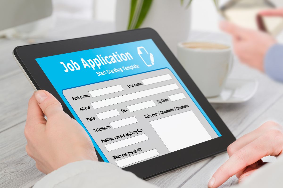 The photo shows a man's hand filling out a job application.