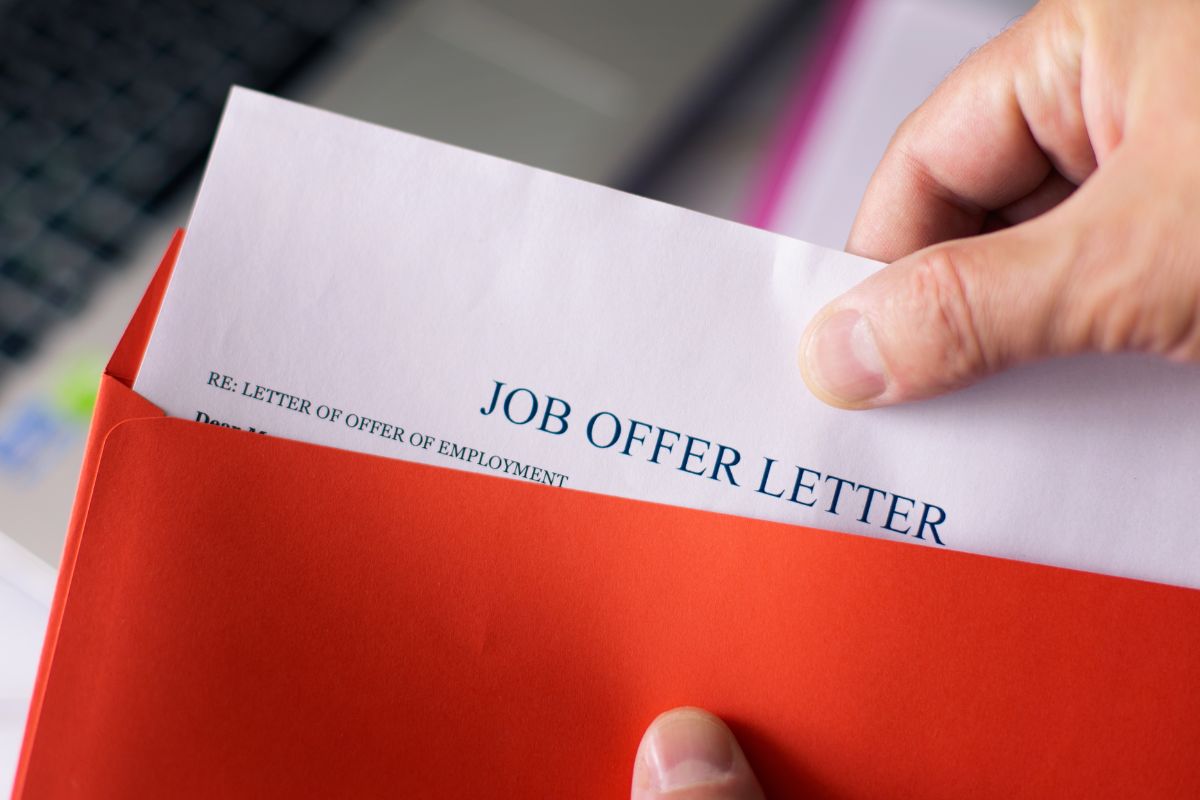 The photo shows a man's hand opening a job offer letter.