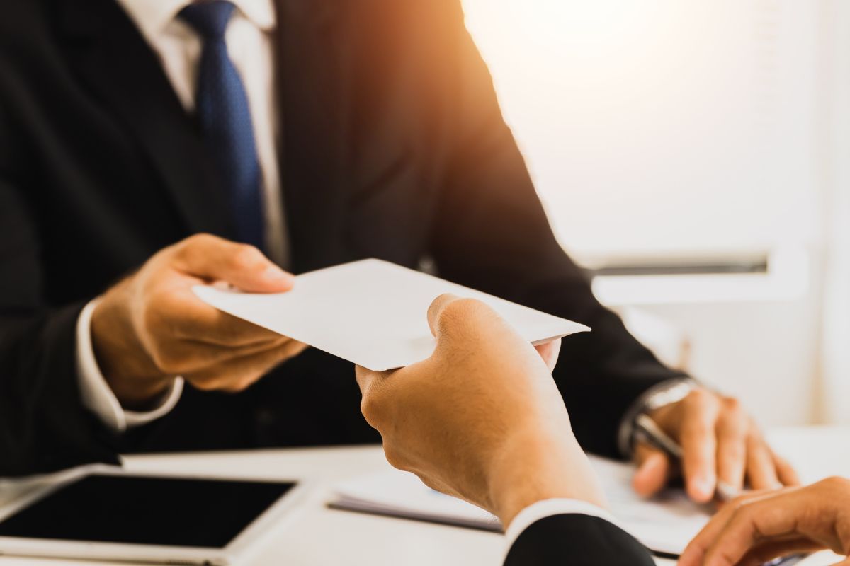 The image tells about a tablet device, papers, and a man giving a white envelope to the man which means saving all unexpected money and making your savings feel effortless.