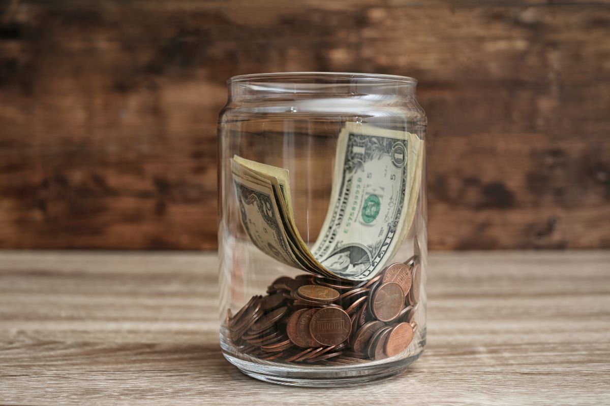The picture shows a jar filled with coins and dollar bills indicating to turn savings into a daily micro habit that can cover emergencies or big goals.