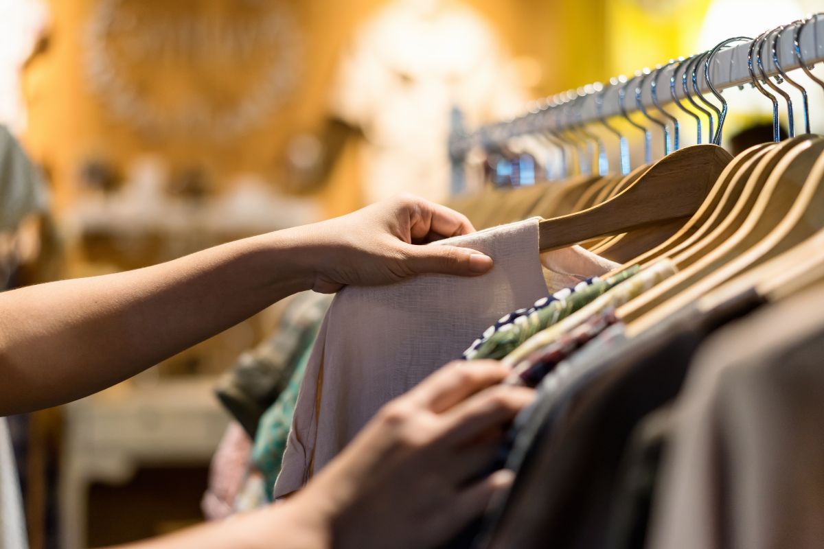 The picture shows a woman choosing clothes in a thrift store.