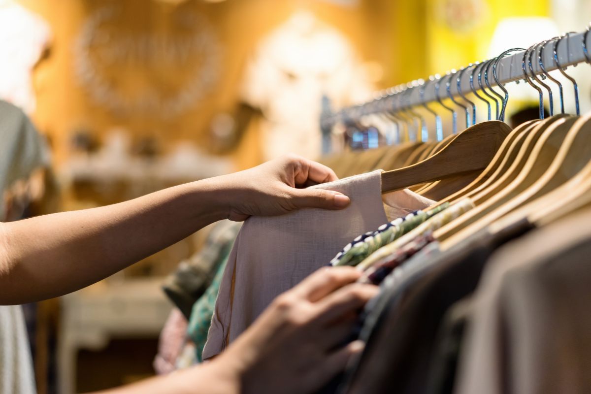 The image tells about a girl's hand picking up clothes which means to flip a thrift store for profit is an easy way to make money fast with a little effort.