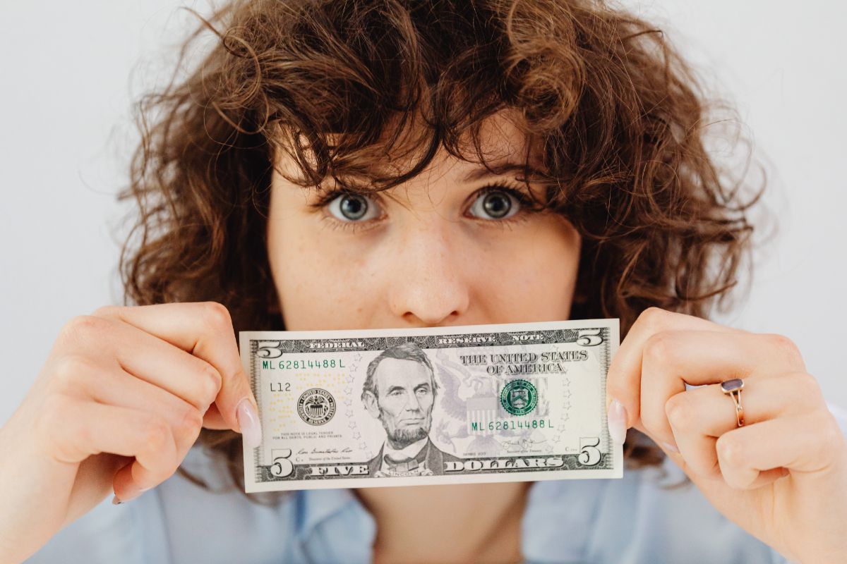 The photo of a girl holding a five-dollar bill which means to charge yourself a convenient tax keeps you aware of your spending while building savings fast.