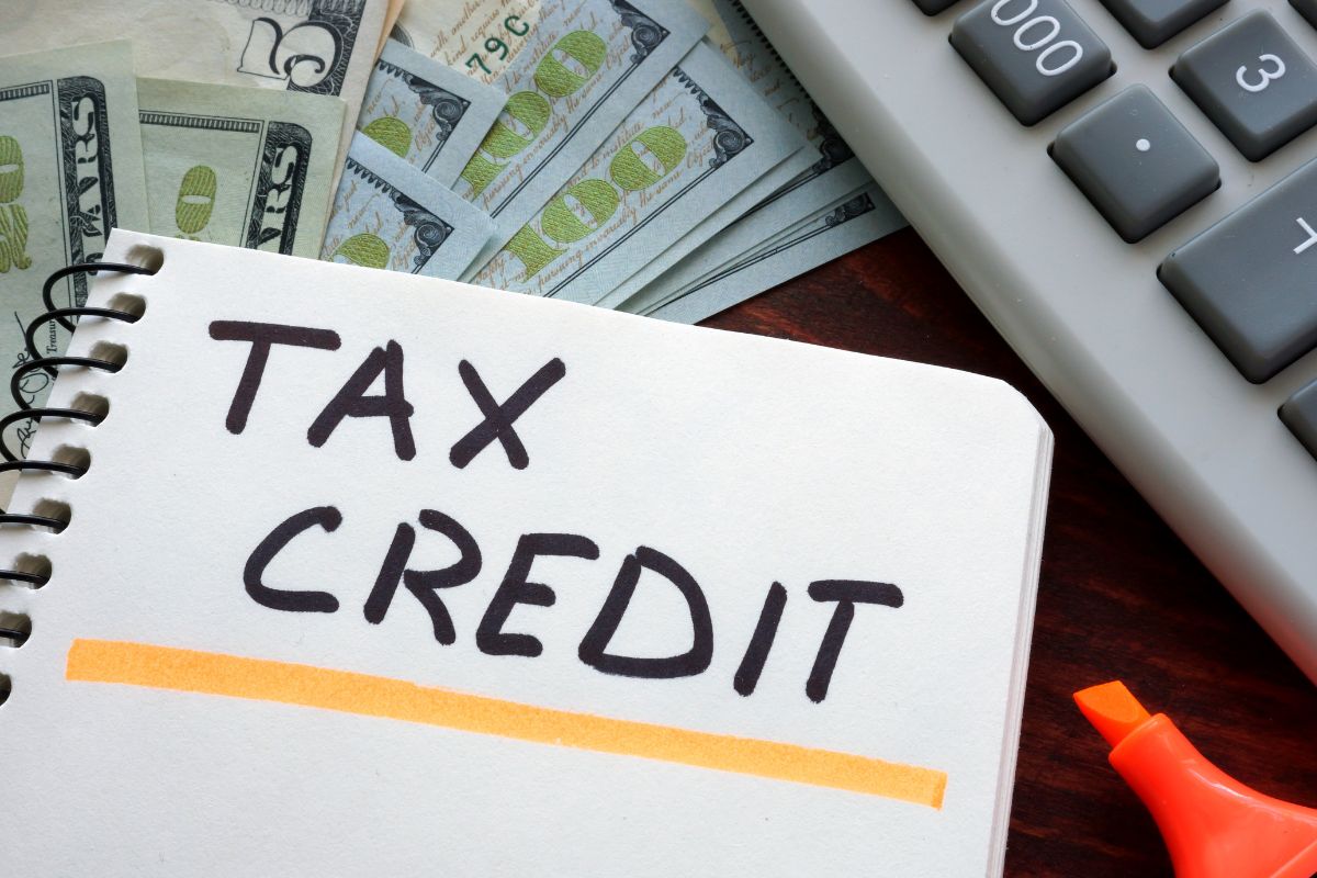 Photo of money, a calculator, and a notebook with tax credit wording.