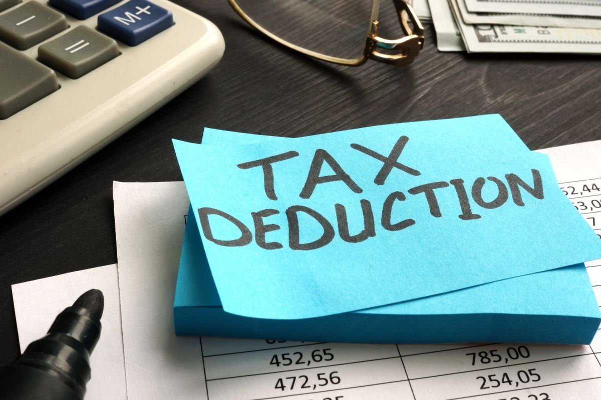 The picture shows a calculator, an eyeglass, dollar bills, and papers with notes and numbers which means to consider bundling deductions into one tax year makes it easier to get the most out of itemized deductions.