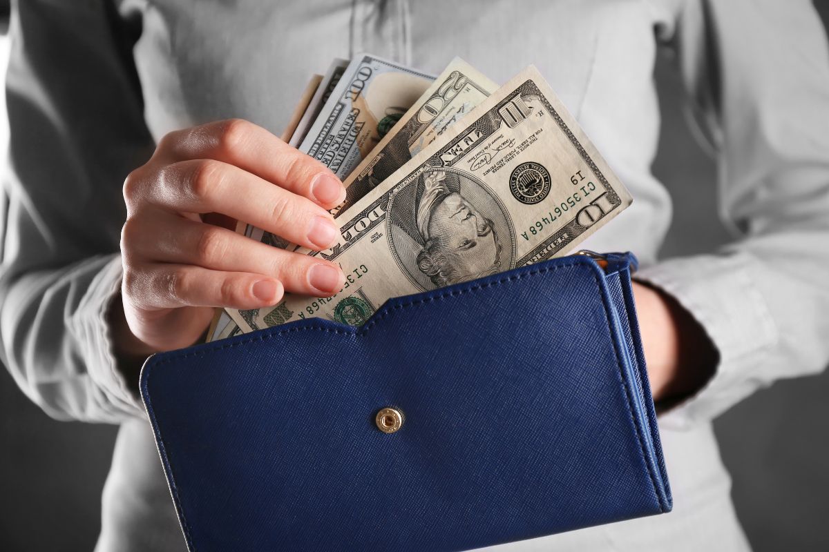 The photo tells about a girl's hand holding a wallet and putting the money inside which means doing a no-spend weekend is an easy way to reach your $500 goal without feeling overwhelmed.