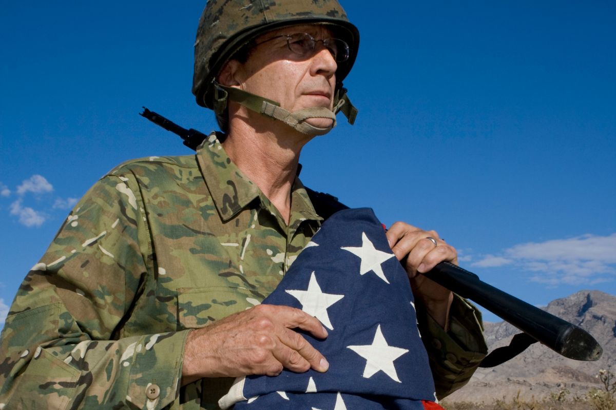 The picture tells about a man in uniform holding a gun and a U.S. flag referring to deducting moving expenses if relocating for military service helps reduce taxable income and ease the financial burden of relocation.