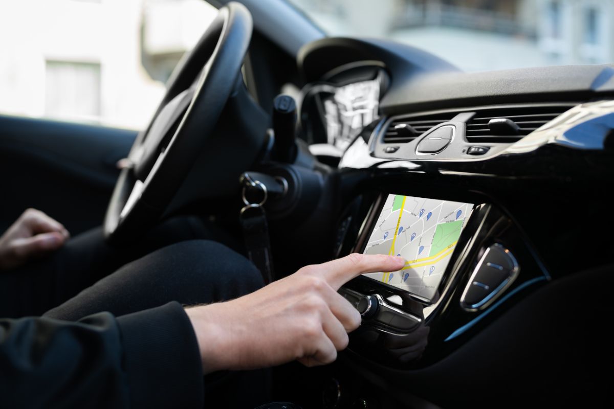 The photo tells about a man's hand in a car using a GPS navigator referring to write off mileage and expenses if using your car for business can lead to significant tax benefits.