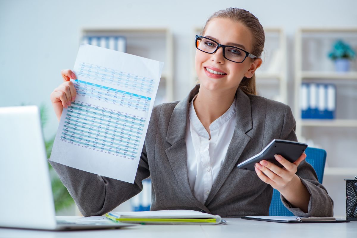 The image tells about a notebook, a laptop, and a girl holding a calculator and a paper which means hiring a tax professional can handle complex situations and can pay less in taxes.