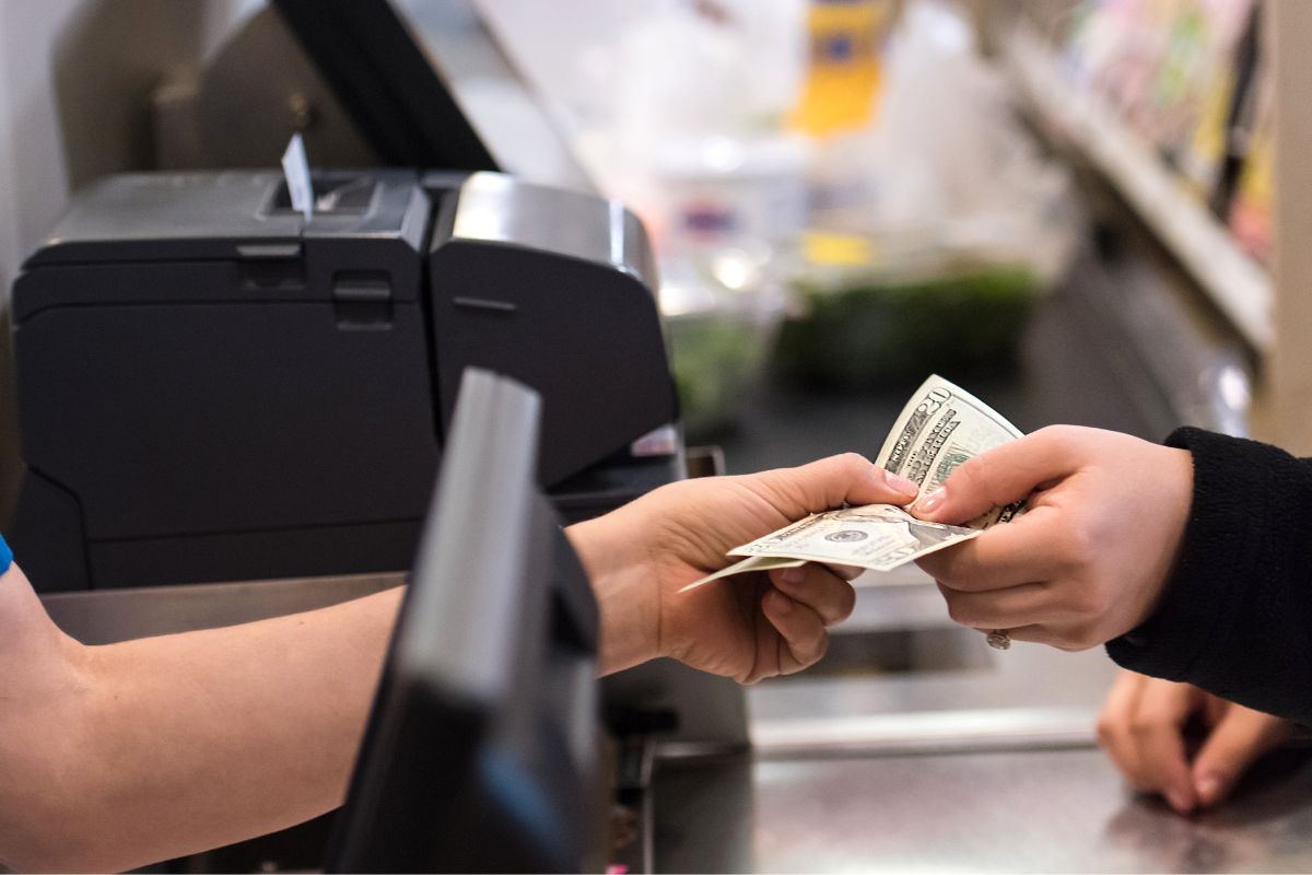 The image shows a woman's hand paying in cash.