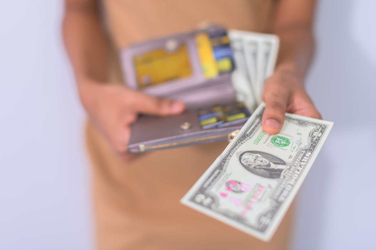 The image tells about a girl's hand holding a wallet and showing off the two-dollar bill indicating that using cash for anything under $20 helps prevent impulse buys.