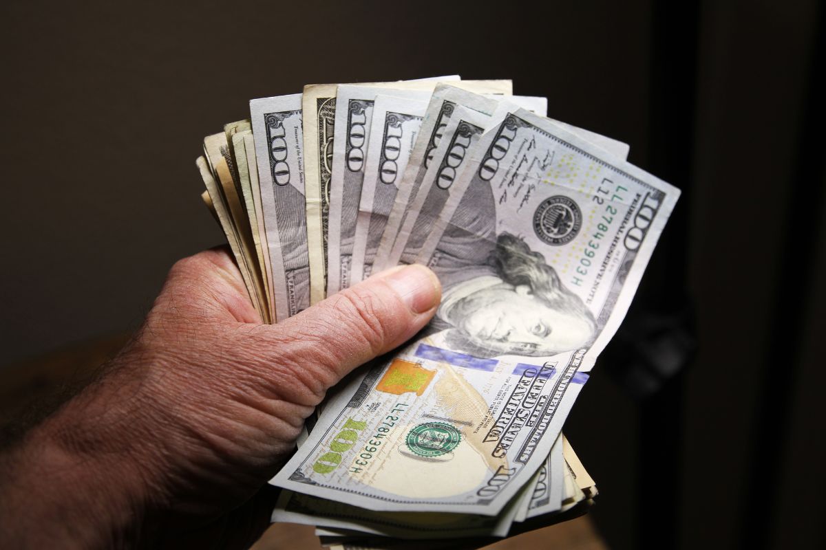 The picture tells about a man's hand holding dollar bills which refers to how much cash should you have on hand to ensure you're never caught off guard.
