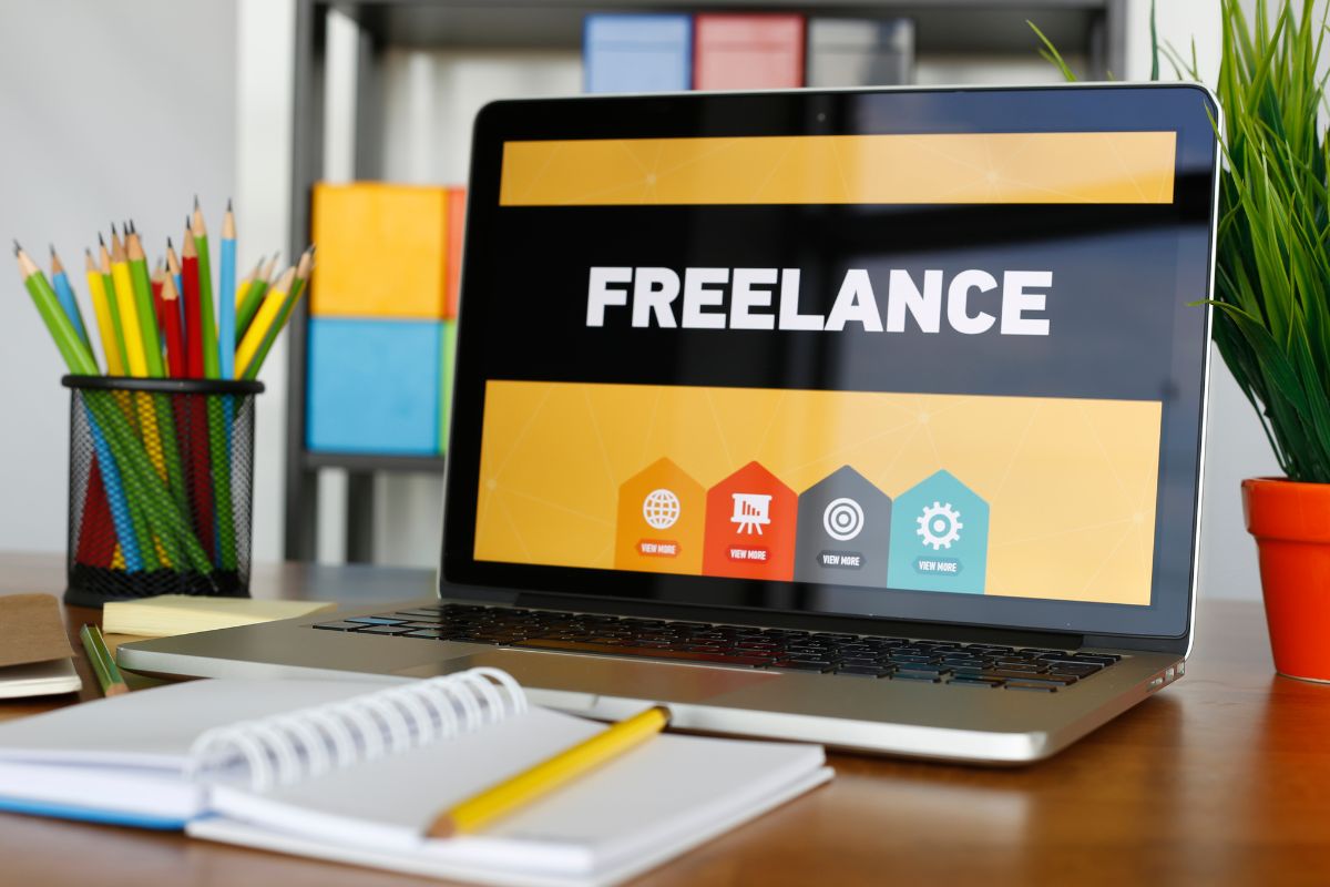The picture shows colored pens, a notebook, a pen, and a laptop with a screen display indicating to offer freelance services on platforms to earn extra cash in your spare time.