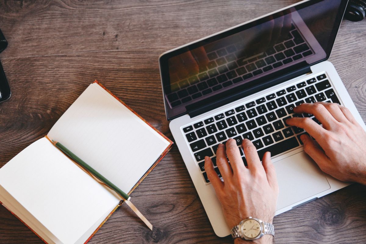 The image shows a man's hand typing on a laptop.