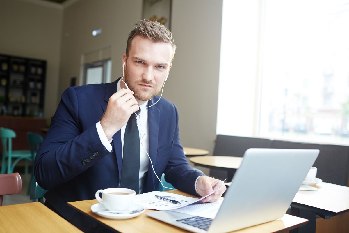 The picture of a man in a suit having a call on the laptop while holding a paper and a coffee on the table which means to become an online business consultant in your area is a flexible way to make money online.
