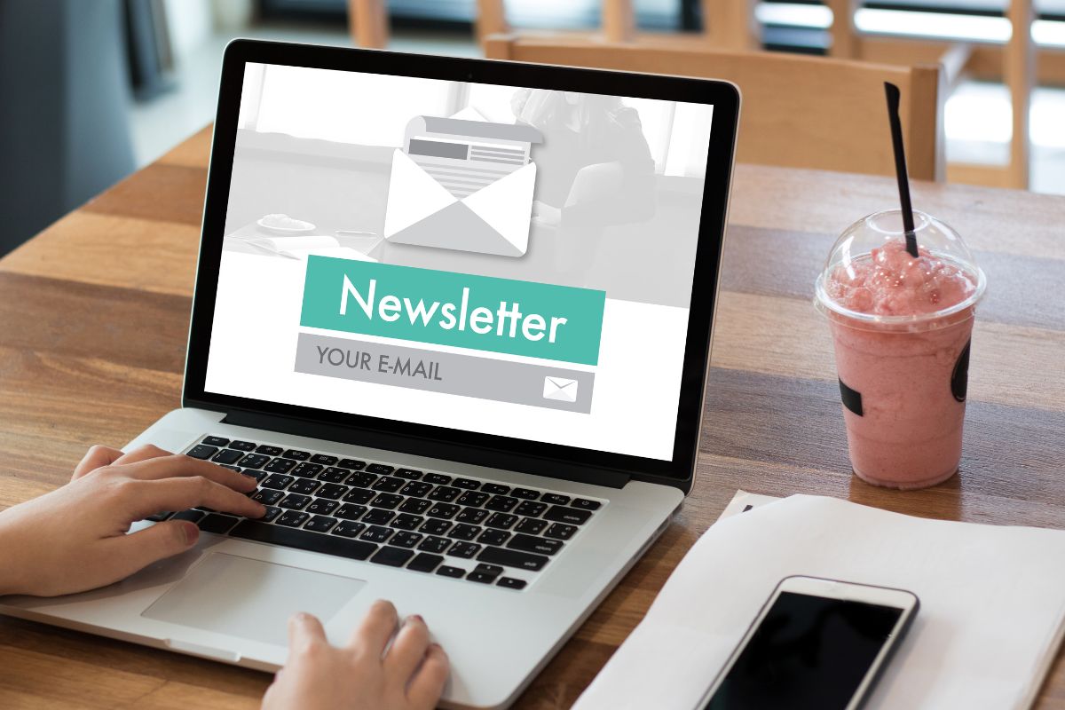 The picture tells about a phone, a piece of paper, a drink, and a girl's hand using a laptop with a screen display indicating that starting a Substack newsletter can be a way to make money online from home and a steady source of income.