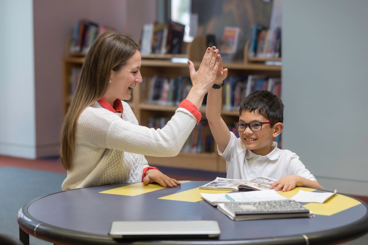 The photo shows papers, a notebook on the table, and a girl doing a high five on her student referring to doing a quick side gig like tutoring is one of the fastest ways to earn extra without long-term commitments.