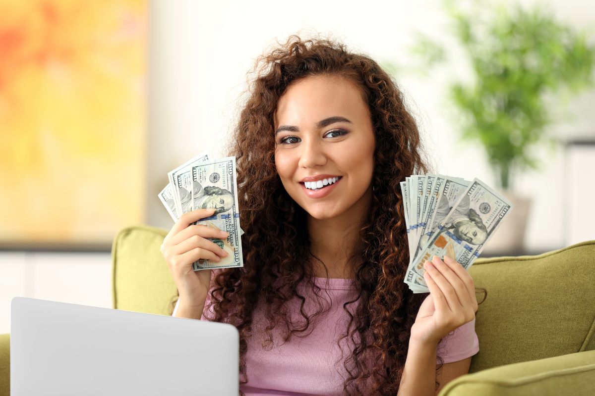 The picture shows a laptop and a girl holding dollar bills referring to finding more ways to make money online for beginners to make extra cash in their spare time.