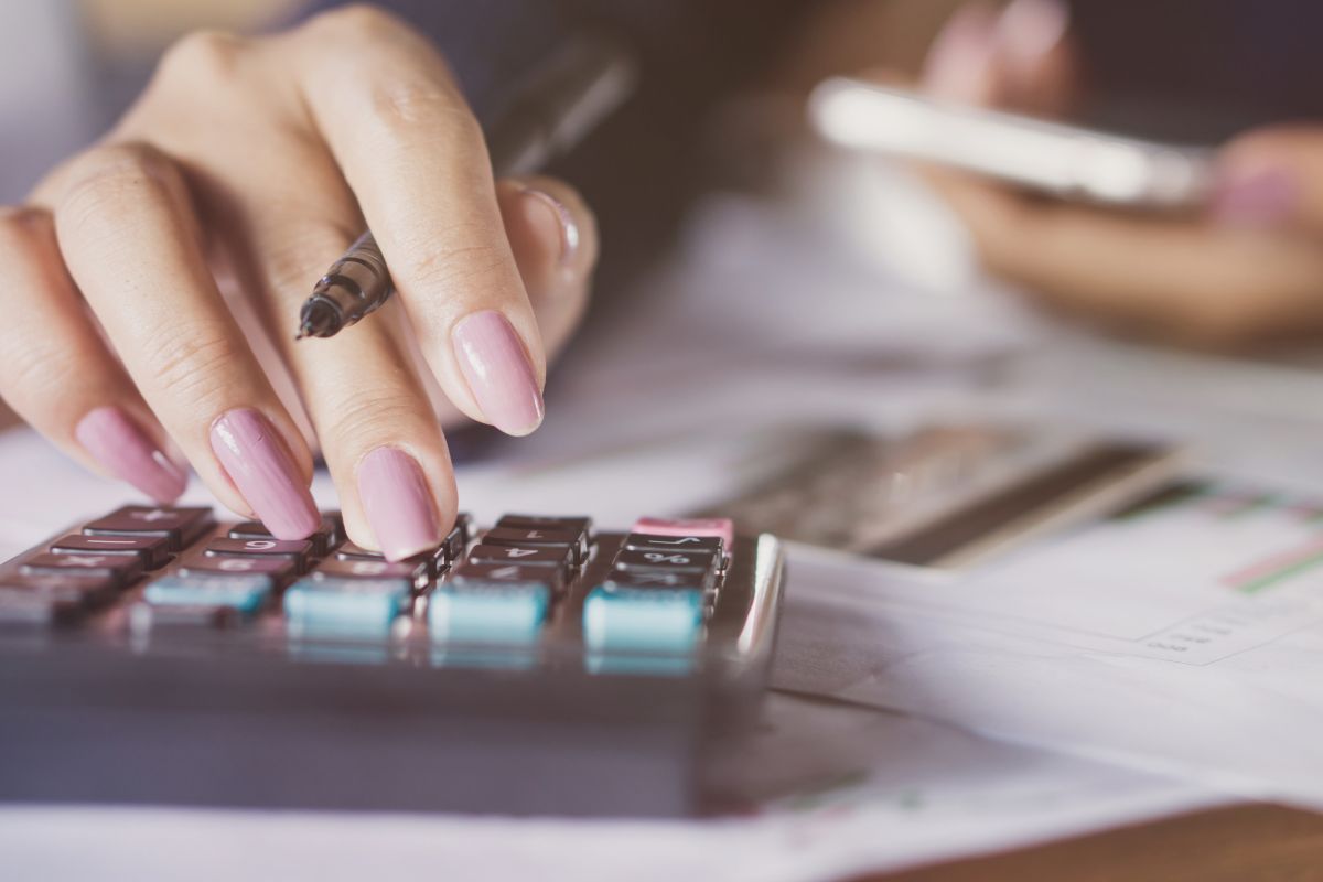 The photo shows papers on the table, credit cards, and a girl's hand calculating while holding a phone referring to calculating your total debt and list balances makes debt payoff less stressful and more effective.