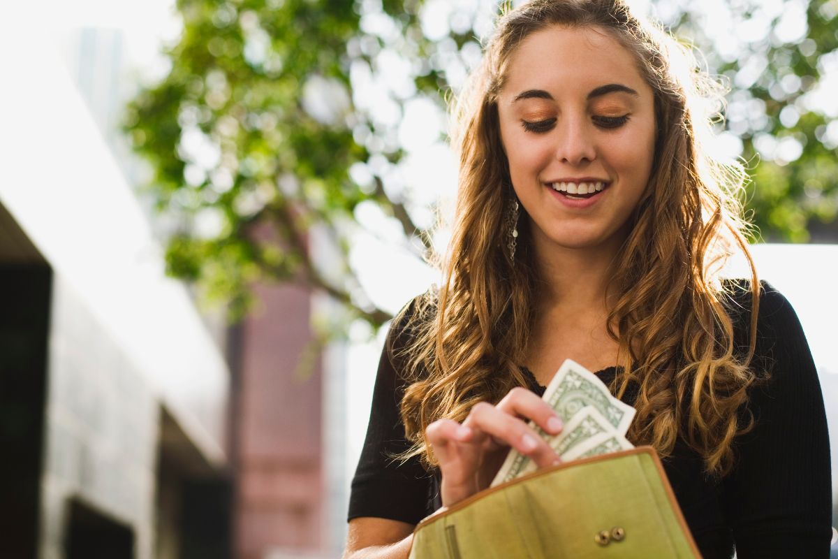 The image tells about a girl putting back the money inside her wallet indicating that challenging yourself to a no-spend week is a simple way to make progress without earning more and speed up debt payoff.