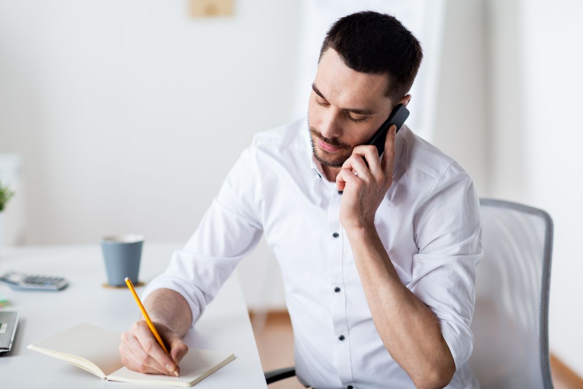 The photo shows a man calling on a photo while taking notes.