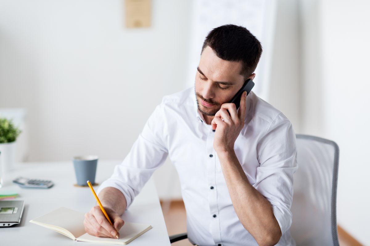 The image shows a man having a call while writing in the notebook referring to calling creditors to negotiate lower interest rates and make debt easier to pay.