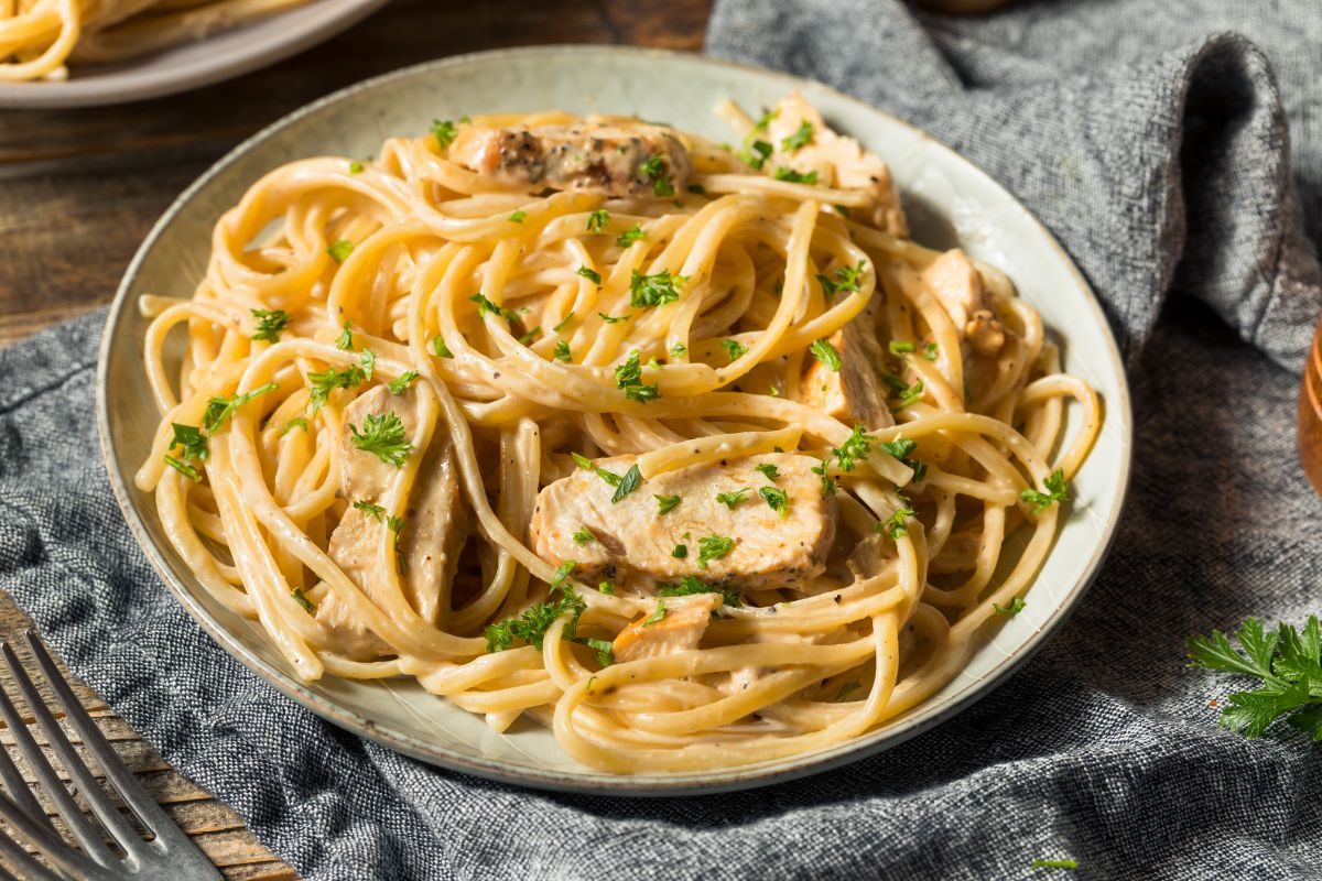 The picture shows a plate with pasta on the table with a fork and fabric referring to rewarding yourself for debt milestones helps you stay committed without slowing your progress.