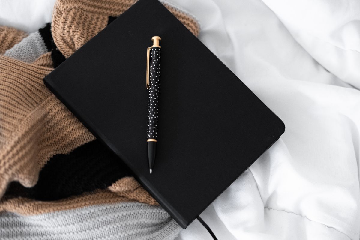 The image shows clothes, a pen, and a notebook which means keeping a journal of how becoming debt-free helps you track progress, stay motivated, and make it easier to keep going.