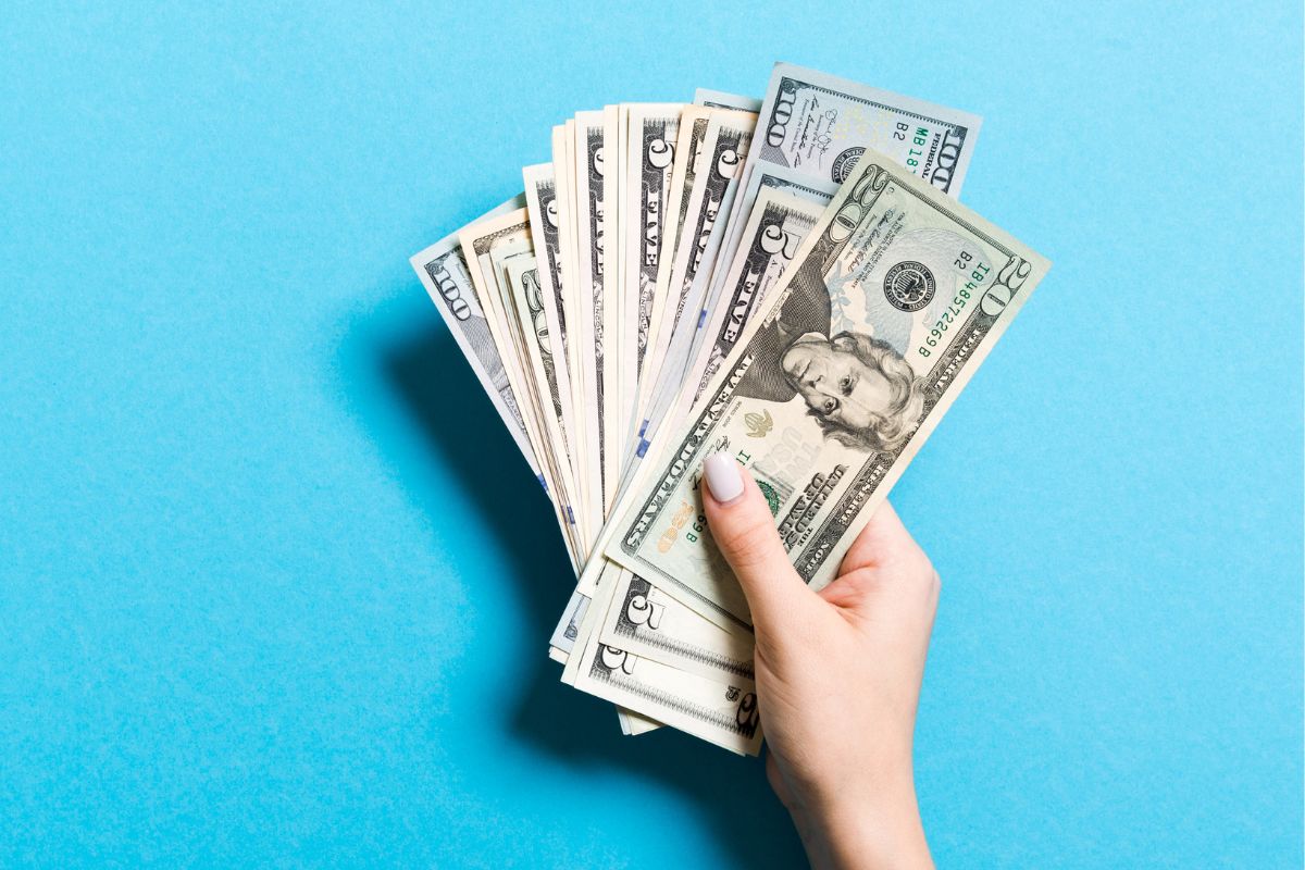 The photo shows a girl's hand holding dollar bills which means using the cash stash trick helps control spending while still allowing room for fun.