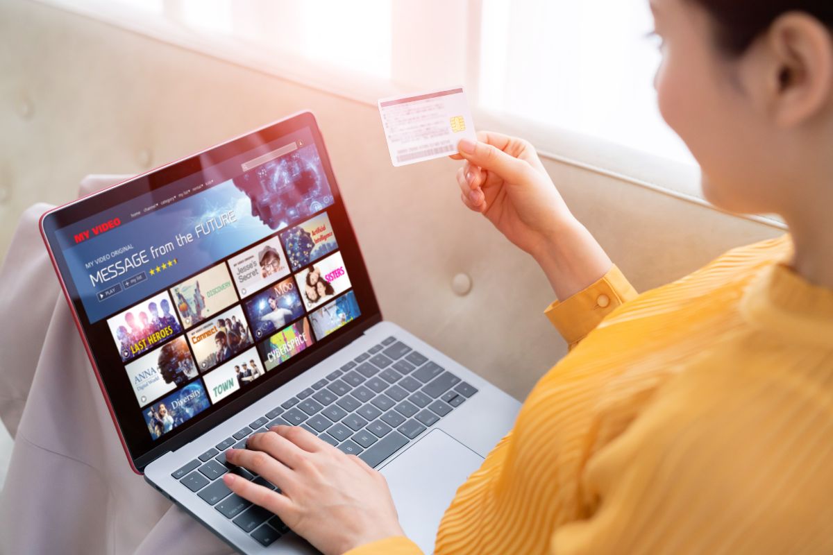 The image shows a girl holding a credit card while using a laptop which means canceling subscriptions creatively makes saving feel effortless.