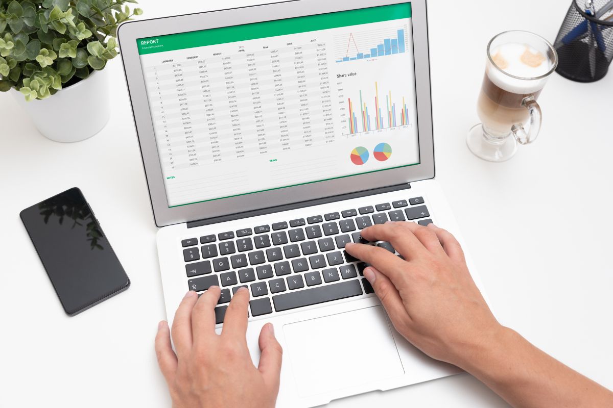The picture tells about a coffee, a phone, and a man's hand using a laptop which means creating a visual debt tracker turns your debt-free goals into something real and achievable.