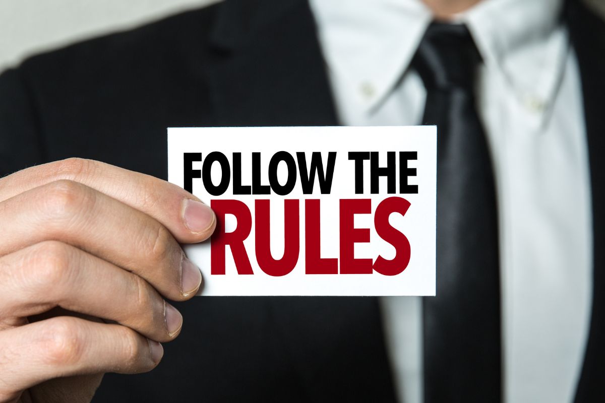 The image shows a man in a suit holding a piece of paper with notes which means following the 50/30/20 rule helps build wealth faster and prevents unnecessary spending.