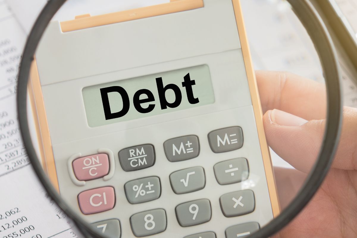 The photo shows a man's hand calculating debt.