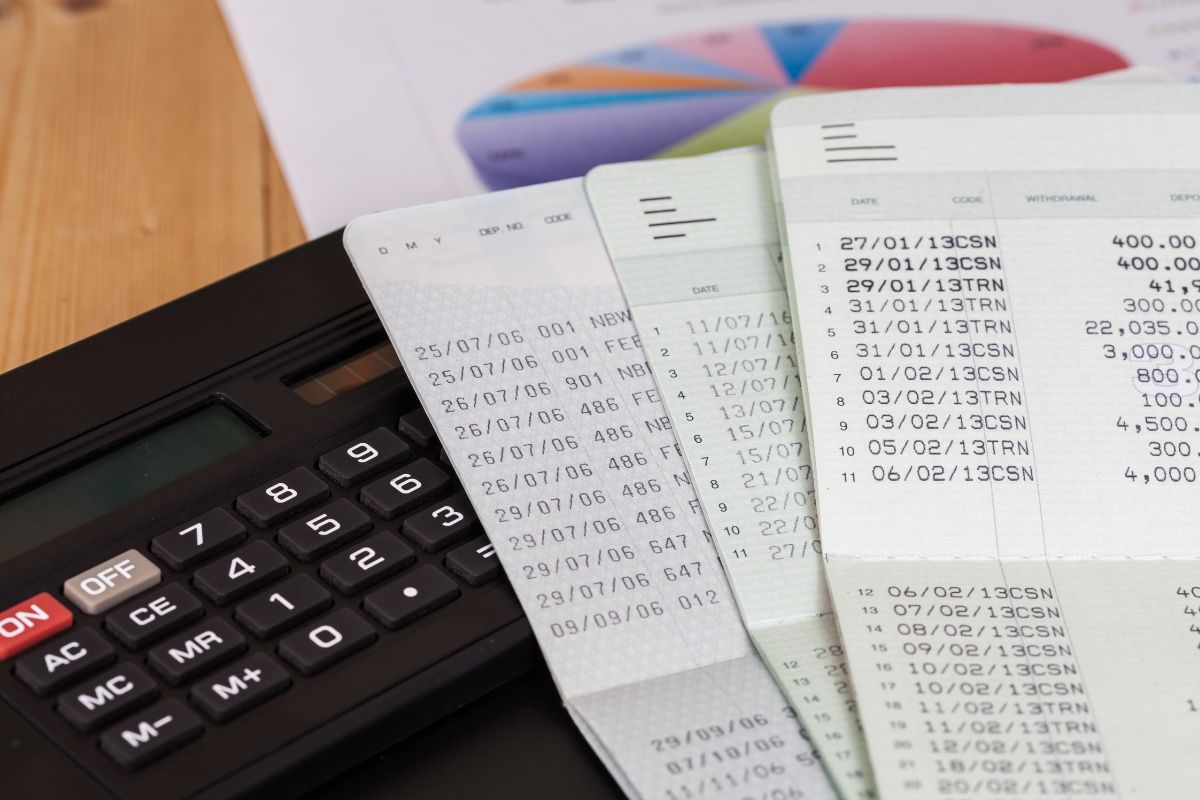 The picture shows papers, a calculator, and bank books indicating that setting up multiple bank accounts prevents accidental overspending and ensures that savings and investments always come first.