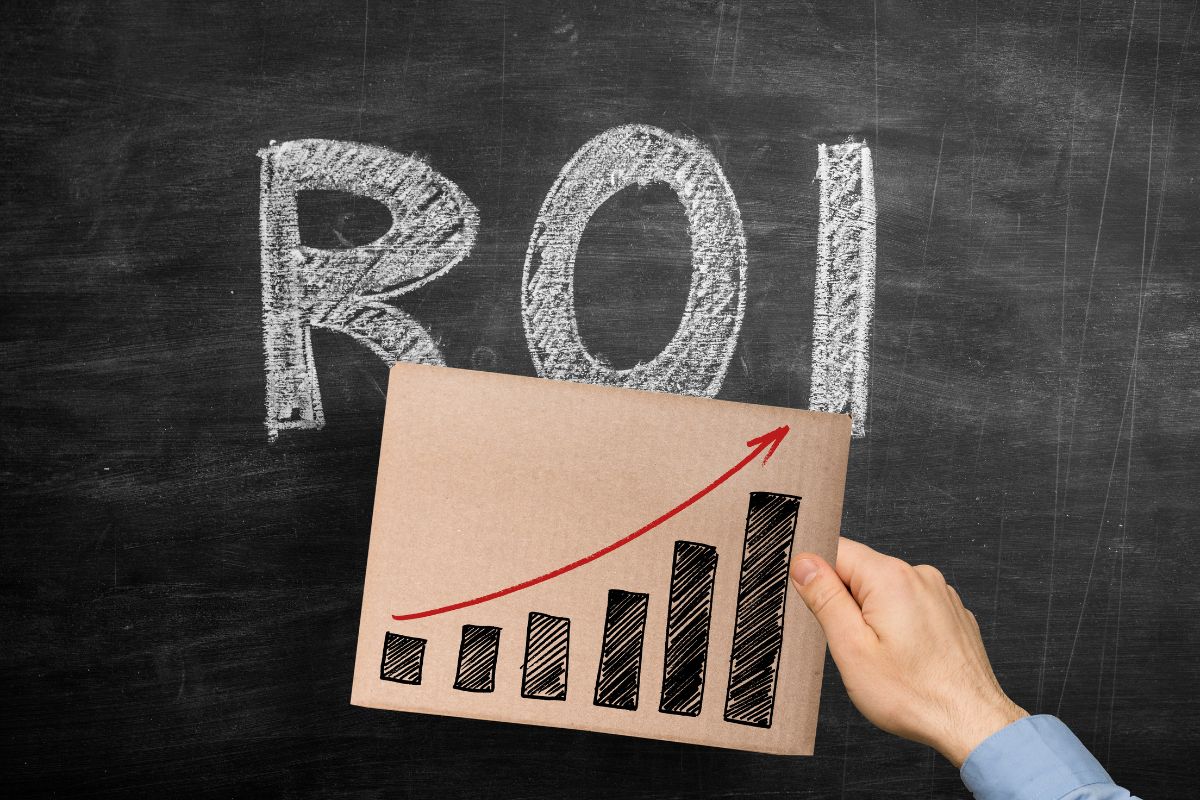 The photo shows a blackboard with letters and a man's hand holding a piece of paper with a graph referring to thinking in ROI that creates financial growth.