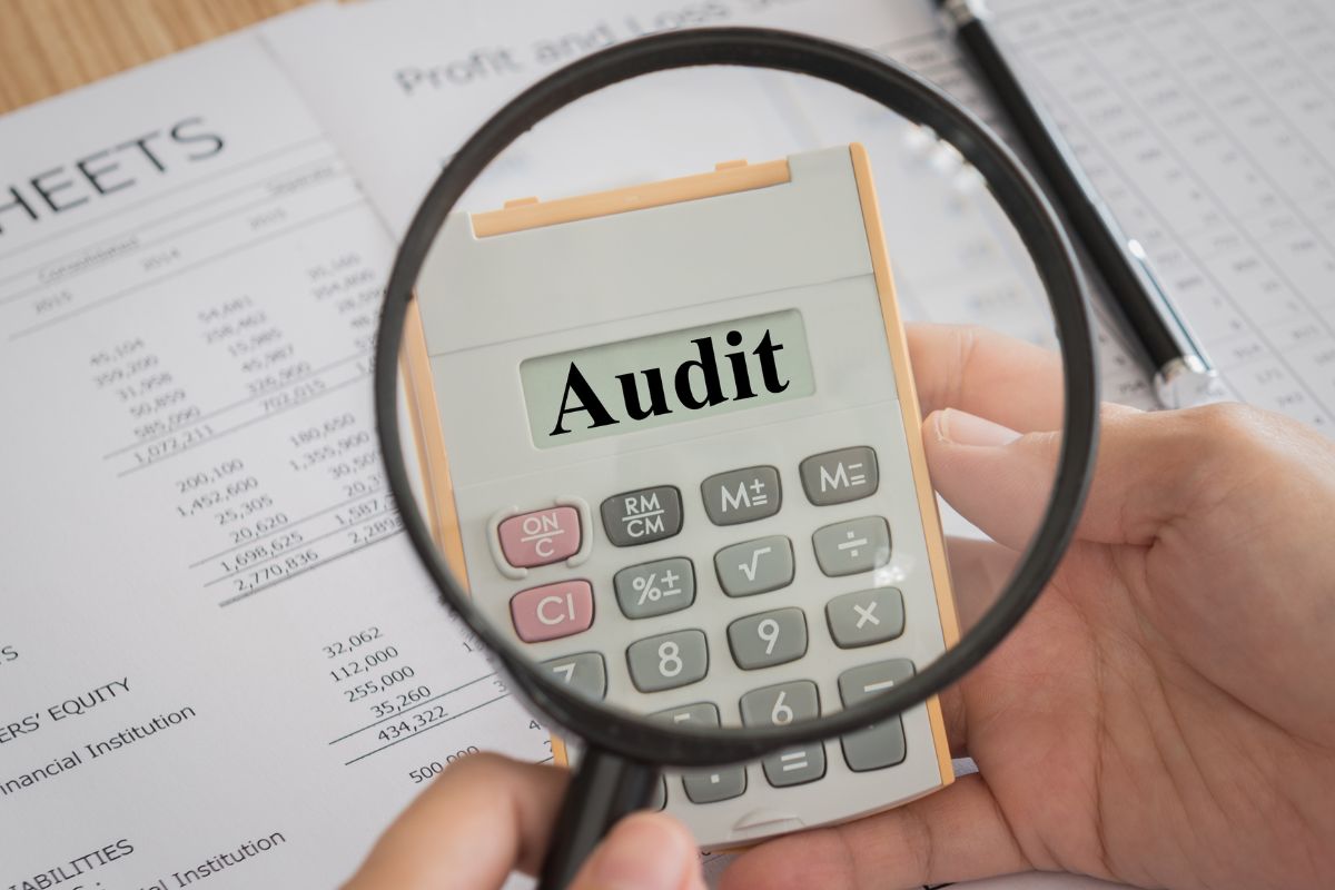 A man's hand using a calculator with audit wording.