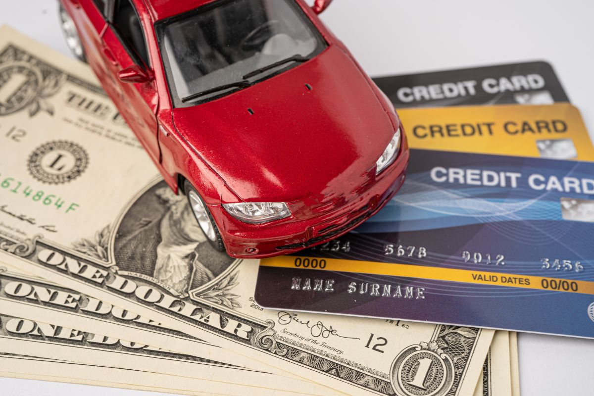 The photo tells about credit cards, dollar bills, and a toy car referring to avoiding financial liabilities as a fast way to stay broke, save first and buy later to keep money free from investments that grow in value.