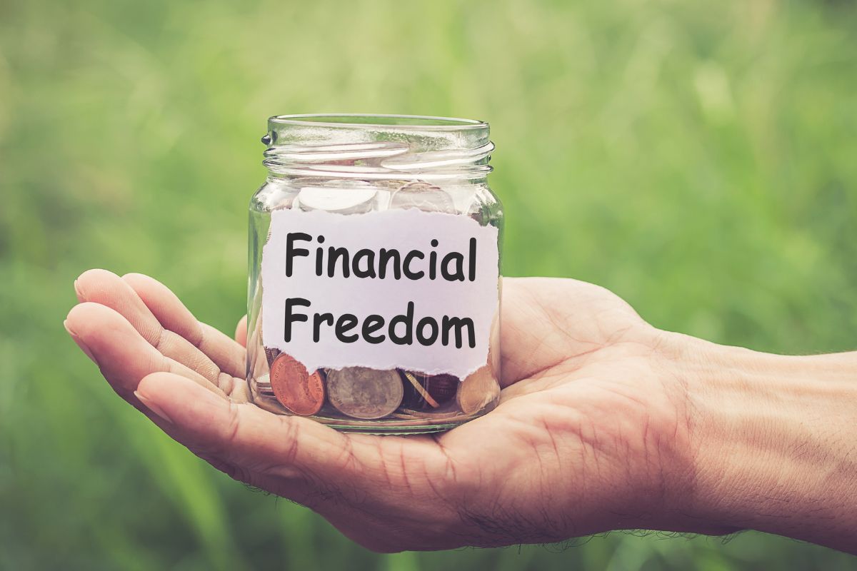 Photo of a man's hand holding a jar with coins and a financial freedom note.
