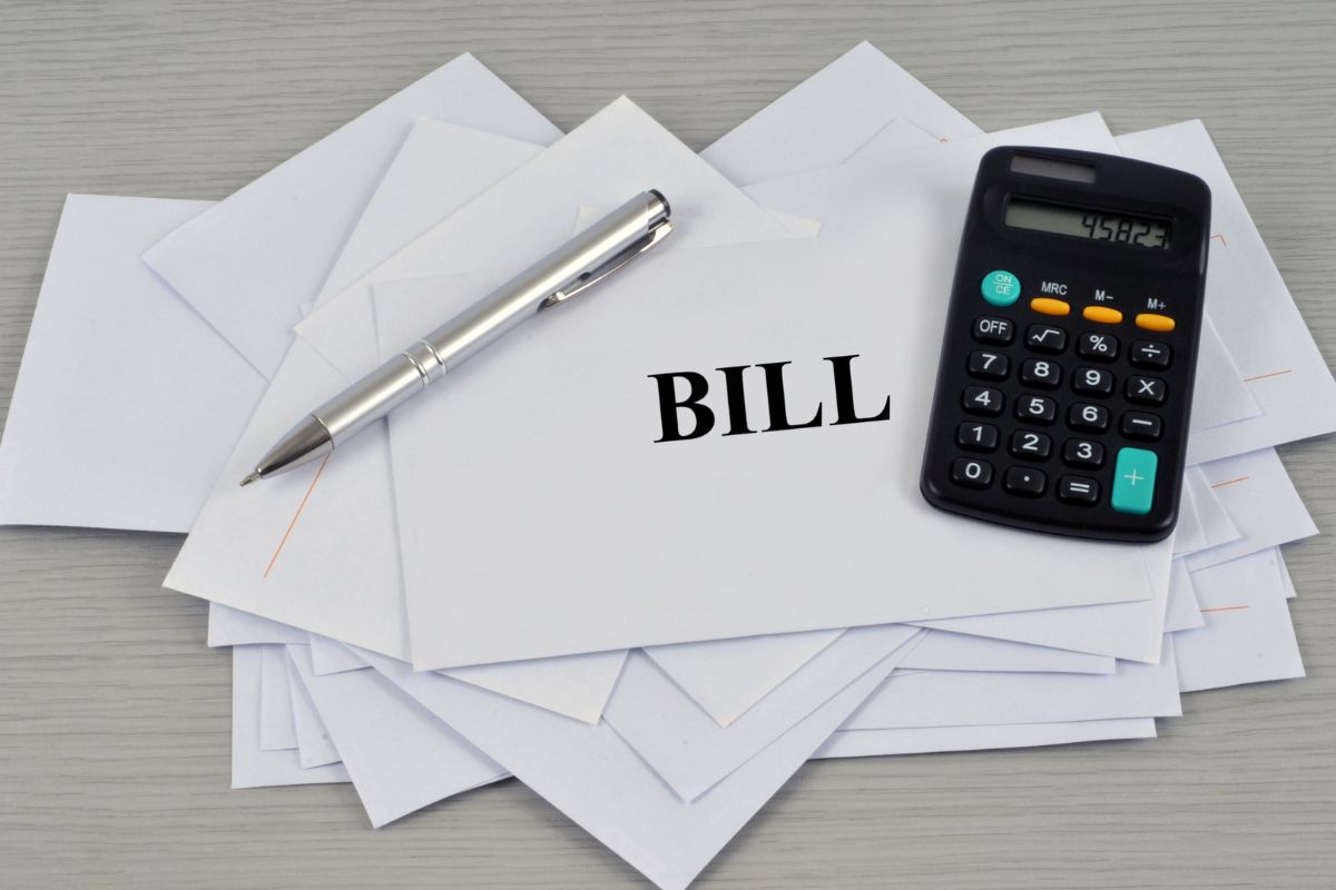 The photo shows a calculator and envelopes with bill wording.