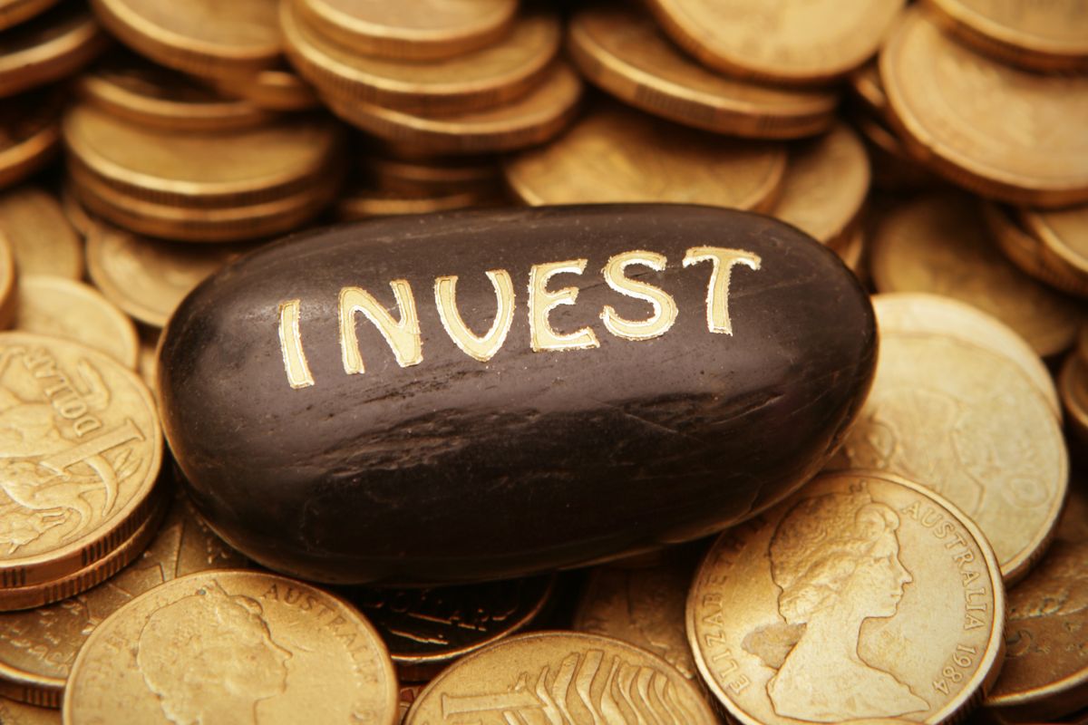 The picture shows coins and a black stone with invest wording.