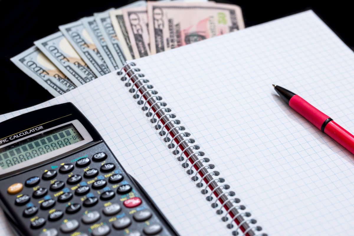 The image shows a calculator, a peen, dollar bills, and a notebook which means that setting clear financial goals helps you make better choices and is easier to say no to things you don't need.