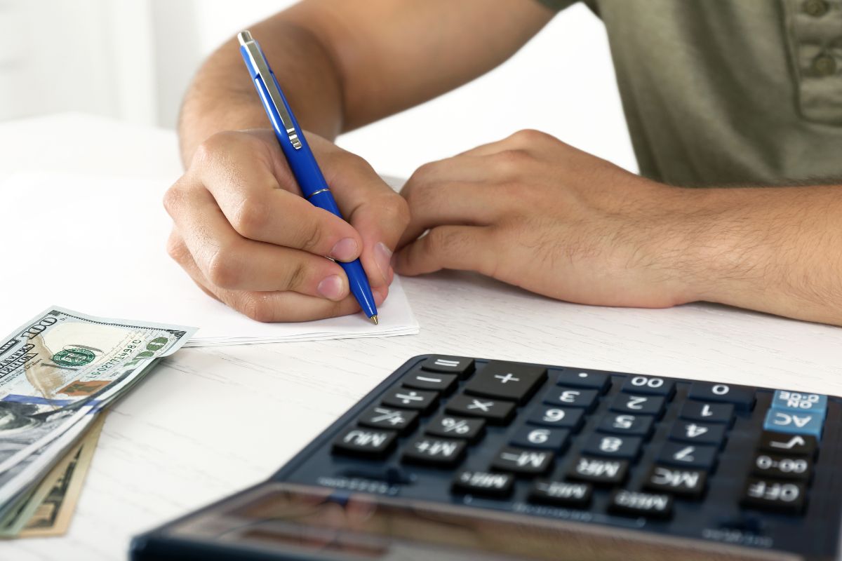 The image shows a calculator, dollar bills, and a man's hand and writing on the paper referring to how choosing a budgeting method helps you stay in control of your spending. 