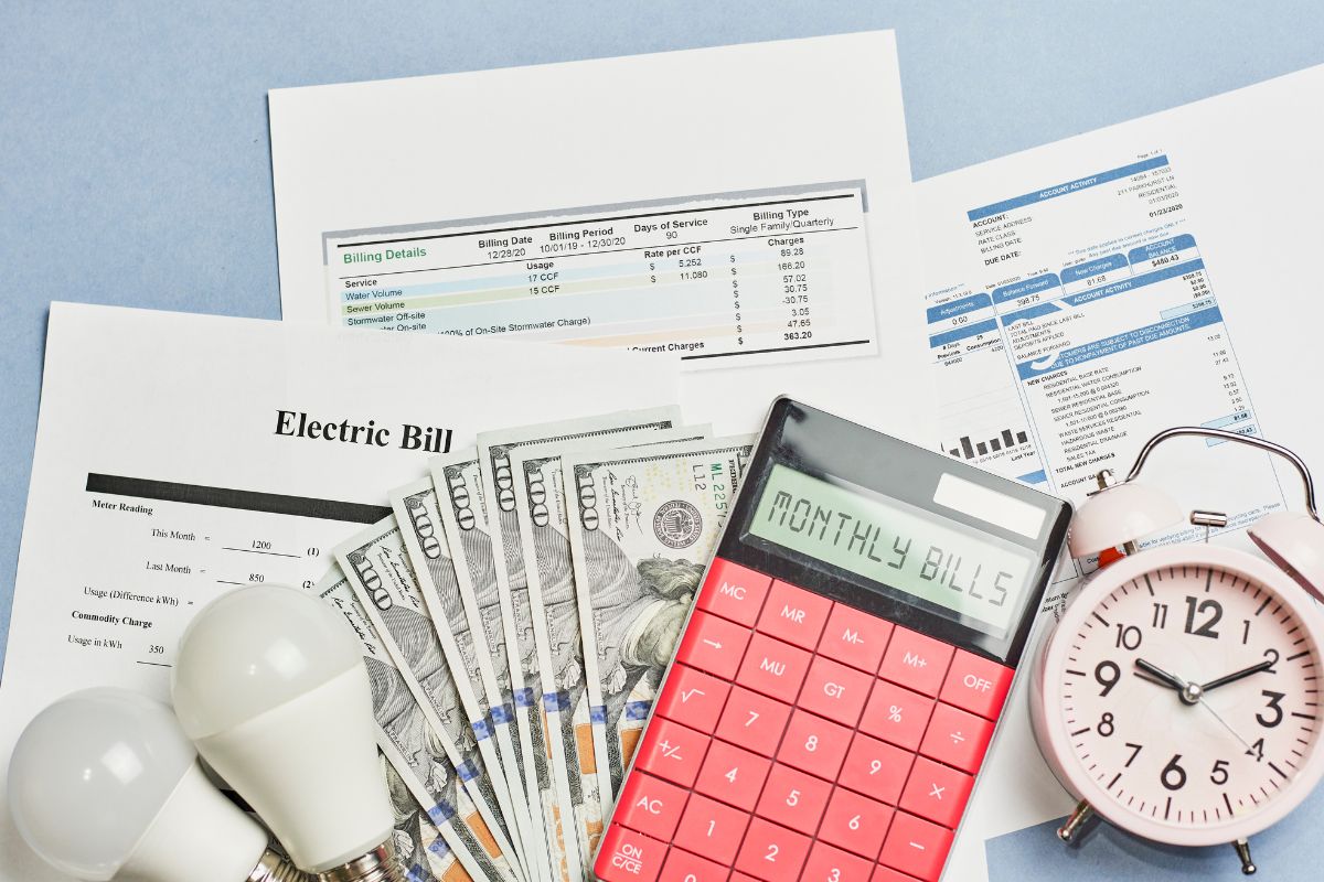 The picture shows bulbs, a clock, a calculator, dollar bills, and papers with notes which refers to automated savings and bill payments that keep you from forgetting and getting hit with late fees.